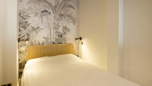 Een slaapkamer met een bed, een wandlamp en een bloemmotief op de muur.