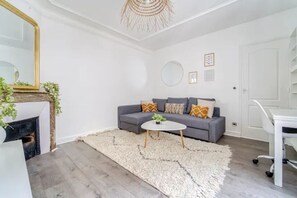 A modern living room with a gray sofa, white coffee table, and a fireplace with greenery.