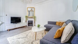 Una sala de estar moderna con un sofá gris, una mesa de centro blanca, un televisor de pantalla plana y una chimenea.