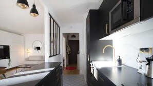 A modern kitchen with dark cabinetry, a black countertop, and stainless steel appliances. - Havre de paix avec balcon (Paris)