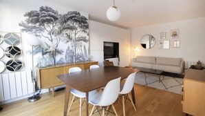 A modern living room with a dining area, featuring a wooden dining table, white chairs, a sofa, and a large abstract painting on the wall. - Havre de paix avec balcon (Paris)