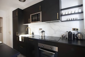 A modern kitchen with dark cabinetry, a stainless steel sink, a microwave, and a coffee machine.