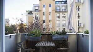 A balcony with a wooden table and chairs, surrounded by potted plants and a view of a multi-story building. - Havre de paix avec balcon (Paris)