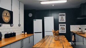 Una cuina moderna amb taula de fusta, armaris blancs i parets negres. Hi ha senyals per a cafè i te, i un cartell de Guinness a la paret.