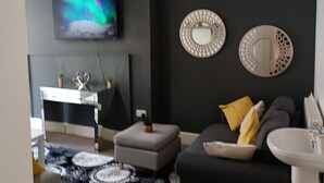 Un saló modern amb un sofà negre, un televisor blanc i miralls decoratius a la paret.