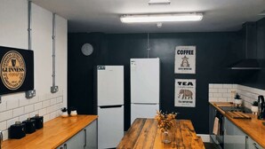 Cuina amb taula de fusta, armaris blancs i paret negra. Hi ha senyals per a cafè i te, i un cartell de Guinness.
