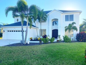 Stunning two-story house with a garage, front entrance, and balcony, set amidst a beautifully manicured lawn and lush greenery.
