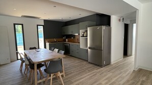 Ett modernt kök med en matplats, utrustat med ett stort bord och stolar, ett kylskåp och en diskmaskin.