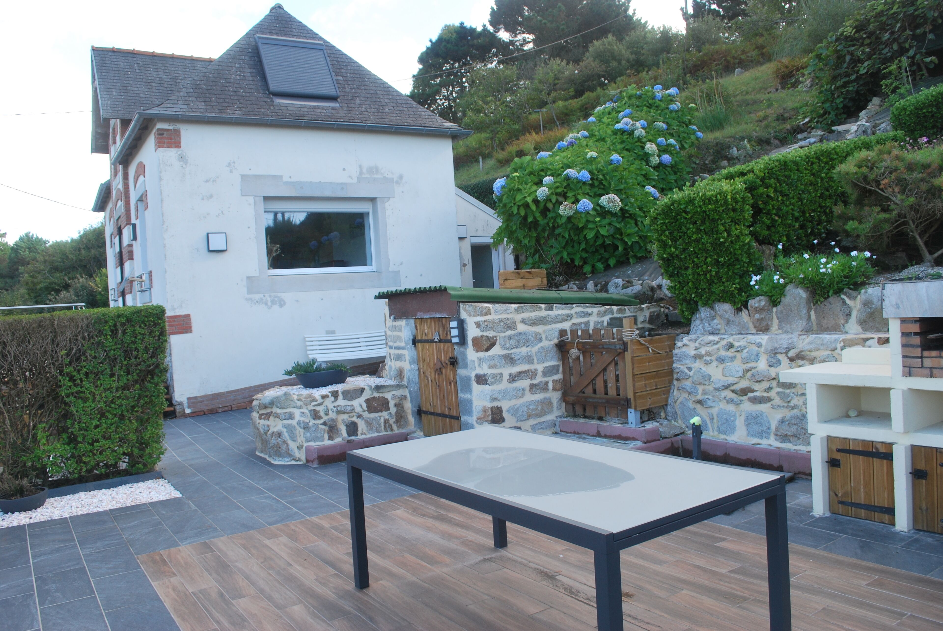 Een huis met een stenen muur, een houten bank en een tafel in de tuin.