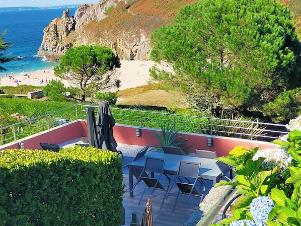 Um terraço com área de estar ao ar livre, vista para a praia e costa rochosa.