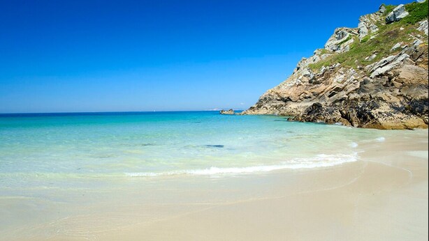 Ein Strand mit klarem türkisblauem Wasser, sandigem Ufer und felsigen Klippen.