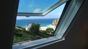 Blick aus einem Fenster auf eine Küstenlandschaft mit blauem Himmel, Felsen und einem Strand.