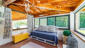 A bedroom with a wooden ceiling, a bed with striped bedding, a yellow dresser, and a large window with a view of greenery. - BEAUTIFUL APARTMENT X 5 WITH HOT-HUB POOL ABOUT 2 KM FROM THE SEA (Imperia)