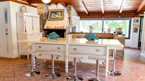 A kitchen with a white island, bar stools, a stone fireplace, and a view of greenery outside. - BEAUTIFUL APARTMENT X 5 WITH HOT-HUB POOL ABOUT 2 KM FROM THE SEA (Imperia)
