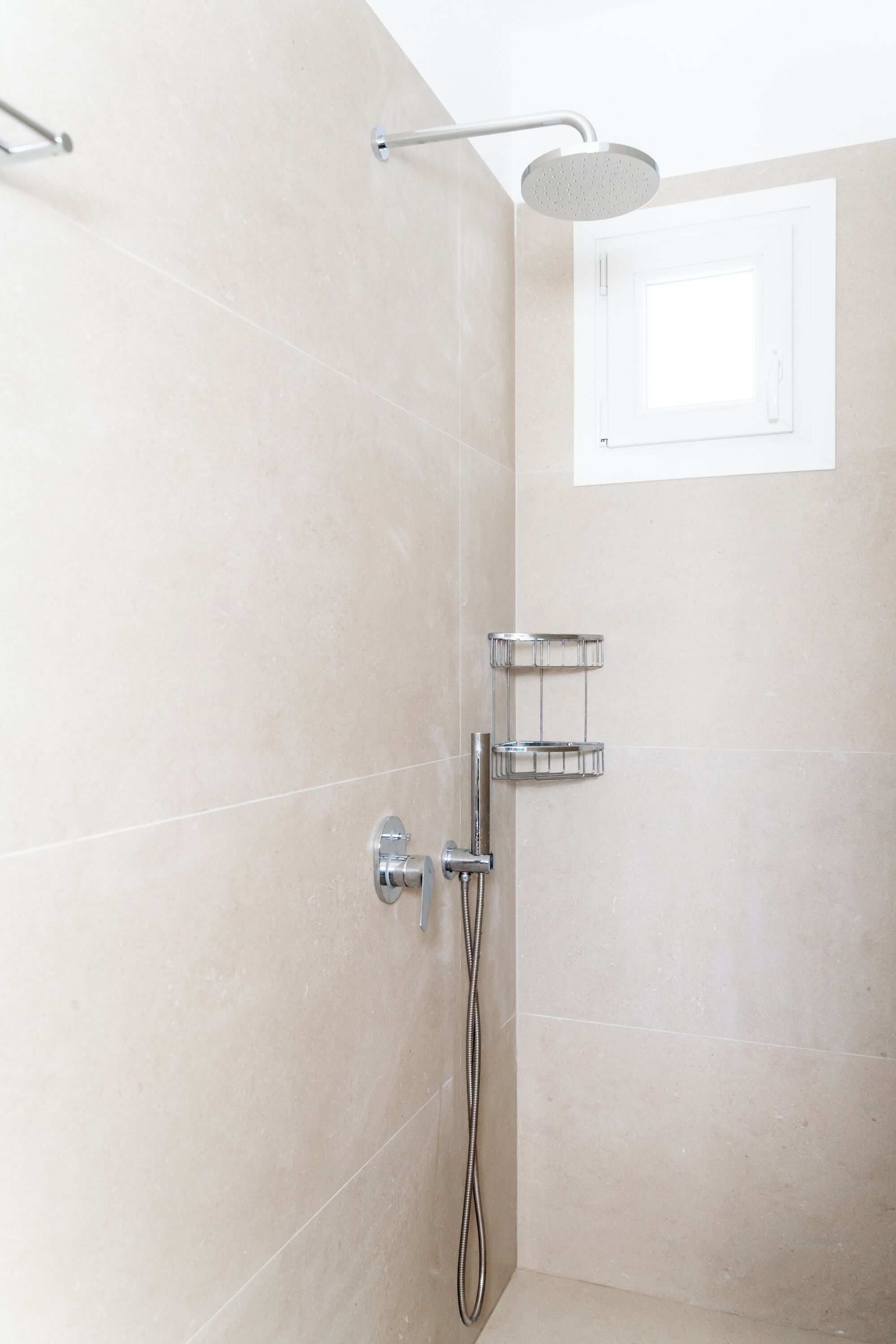 Une douche équipée d’un pommeau de douche à main, d’un robinet mural et d’un porte-serviettes en chrome.