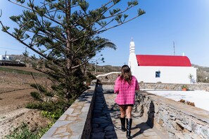 Uma passagem que leva a um edifício branco com telhado vermelho, cercado por vegetação e uma parede de pedra.