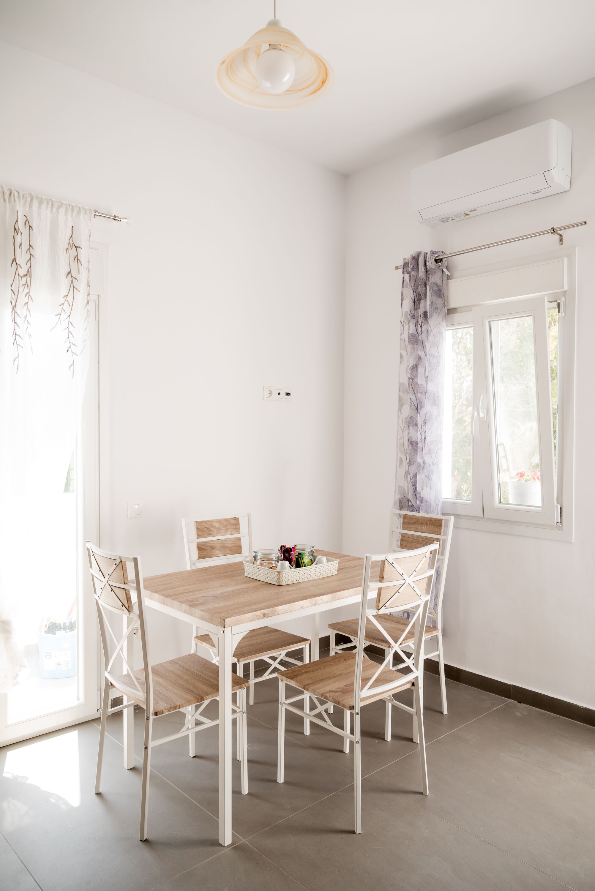 A dining area with a wooden table and white chairs, a pendant light, and a window with curtains.