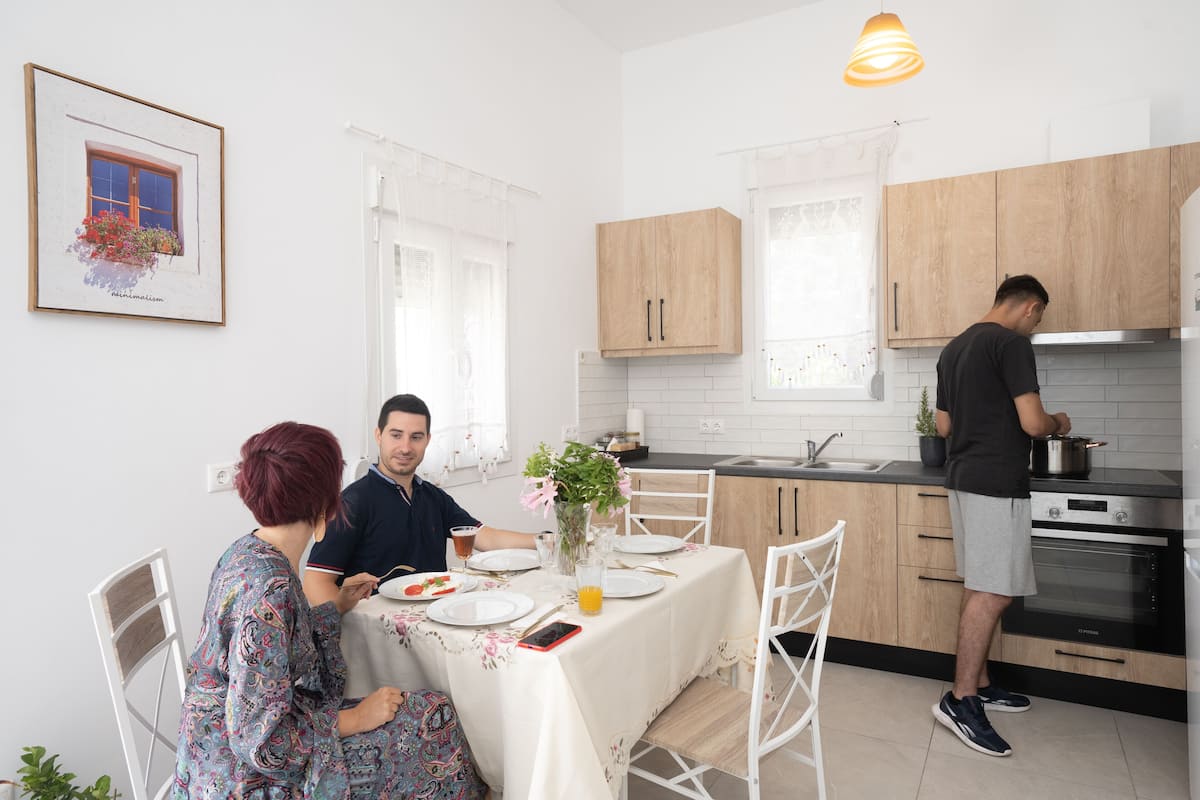 Eine moderne Küche mit Holzschränken, einem Edelstahlbackofen und einem Essbereich mit Tisch für zwei Personen.