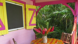 Un pequeño patio con una mesa y sillas, una planta en maceta y una ventana con contraventanas.