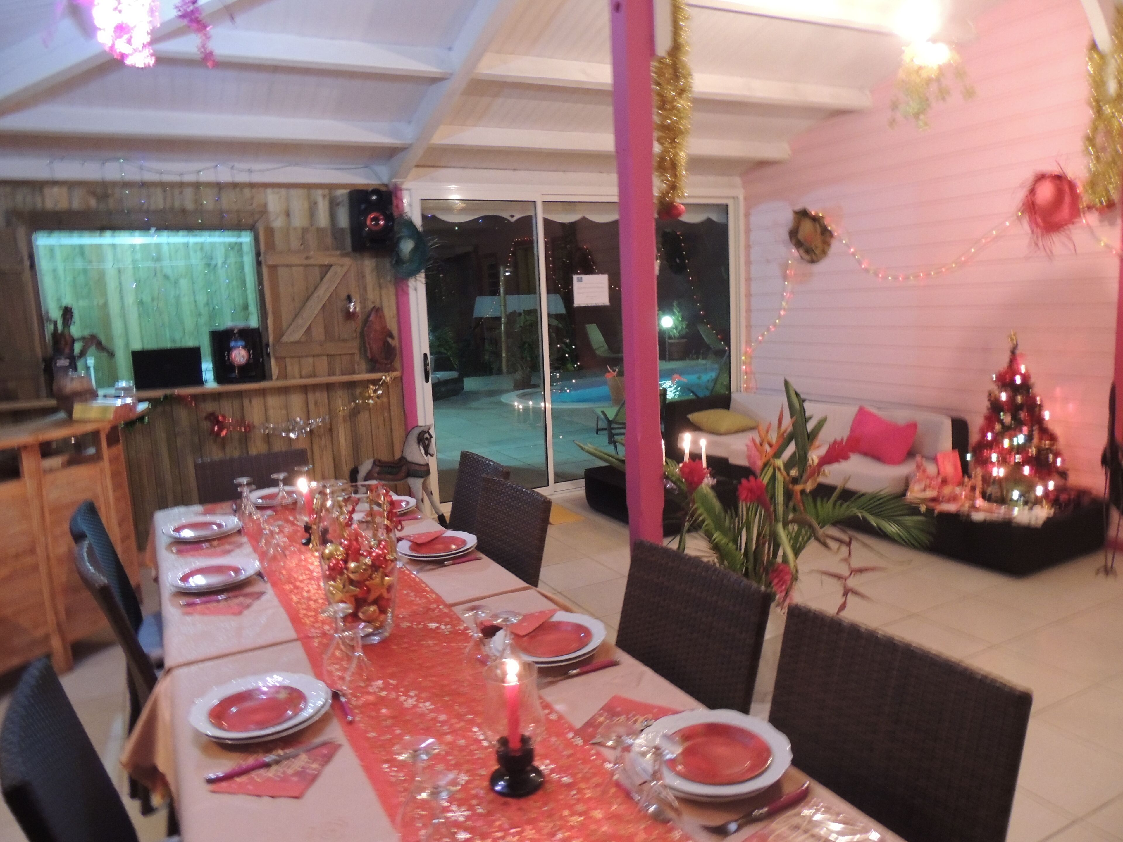 Un comedor con una larga mesa dispuesta para una comida, un árbol de Navidad y una piscina al fondo.