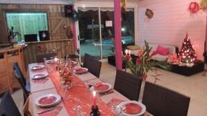 Un comedor con una larga mesa dispuesta para una comida, un árbol de Navidad y una piscina al fondo.