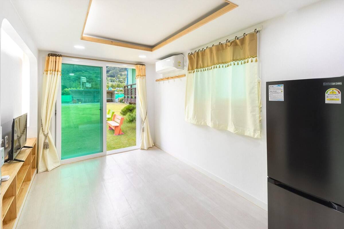 A modern kitchen with a black refrigerator, a sliding glass door leading to a garden, and a wooden bench with a TV.