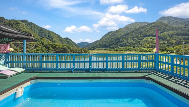 A pool with a blue railing, surrounded by lush green hills and a clear sky.