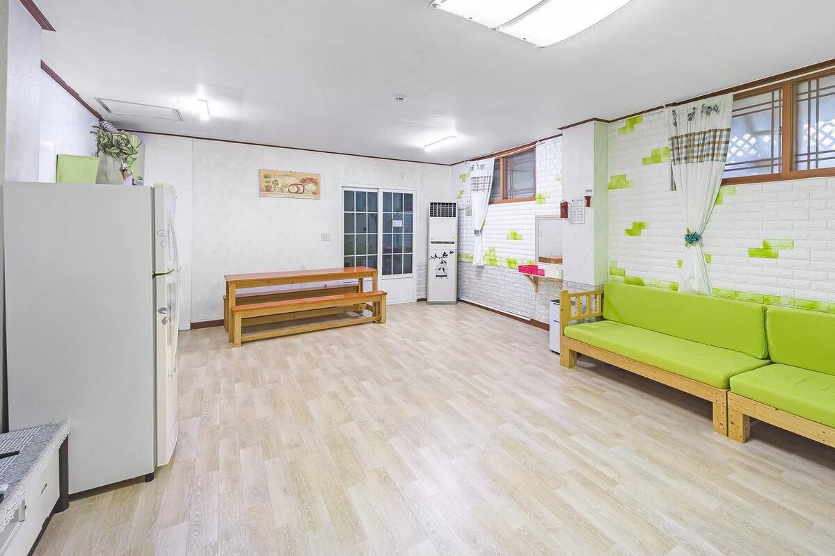 A room with a wooden bench, a green sofa, a white refrigerator, and a window with a view of a fence.