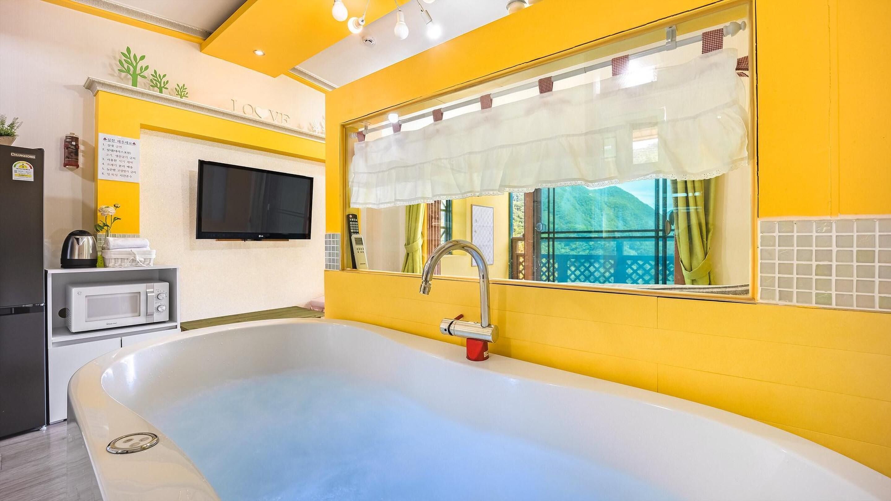 A bathroom with a bathtub, a sink, a microwave, and a television.