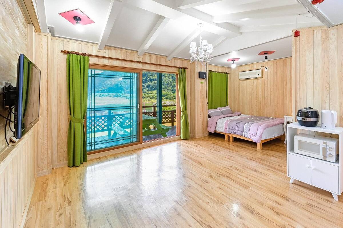 A bedroom with a bed, a small white cabinet, a ceiling fan, and a view of a balcony.
