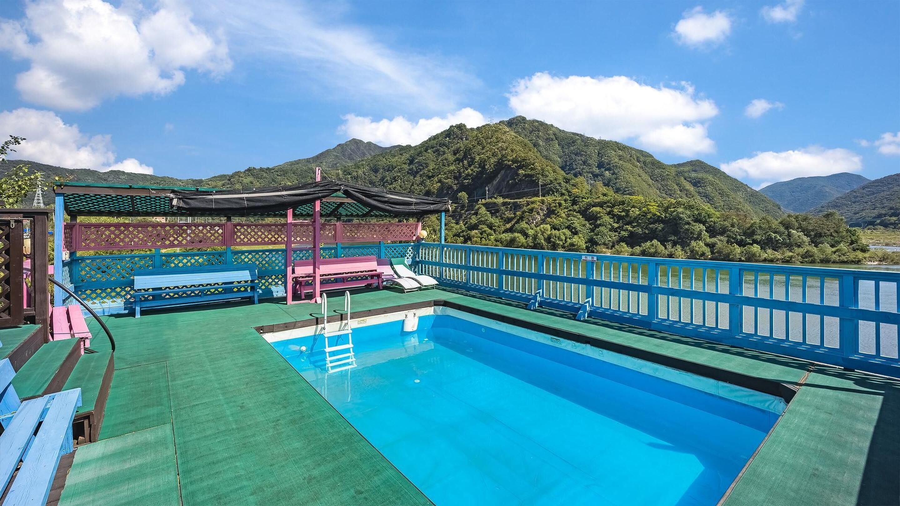 A pool area with a view of mountains, a covered seating area, and a blue railing.