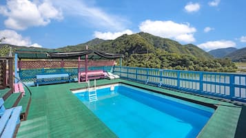 A pool area with a view of mountains, a covered seating area, and a blue railing.