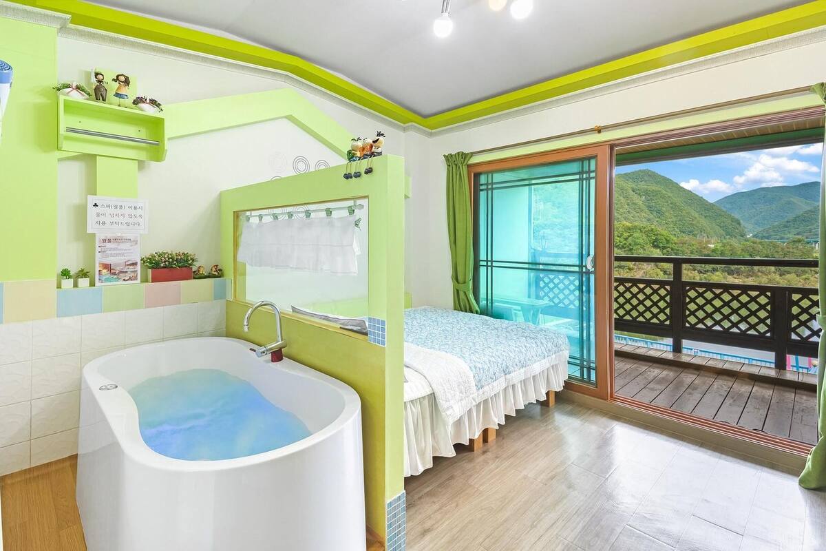 A bathroom with a bathtub, a shower, and a toilet. There is a bed with a view of the mountains.