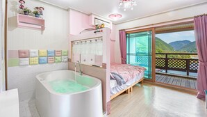 A bedroom with a large window, a bathtub, and a balcony with a view of the mountains.