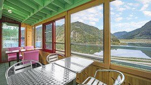 A room with large windows, a table, chairs, and a view of a lake and mountains.
