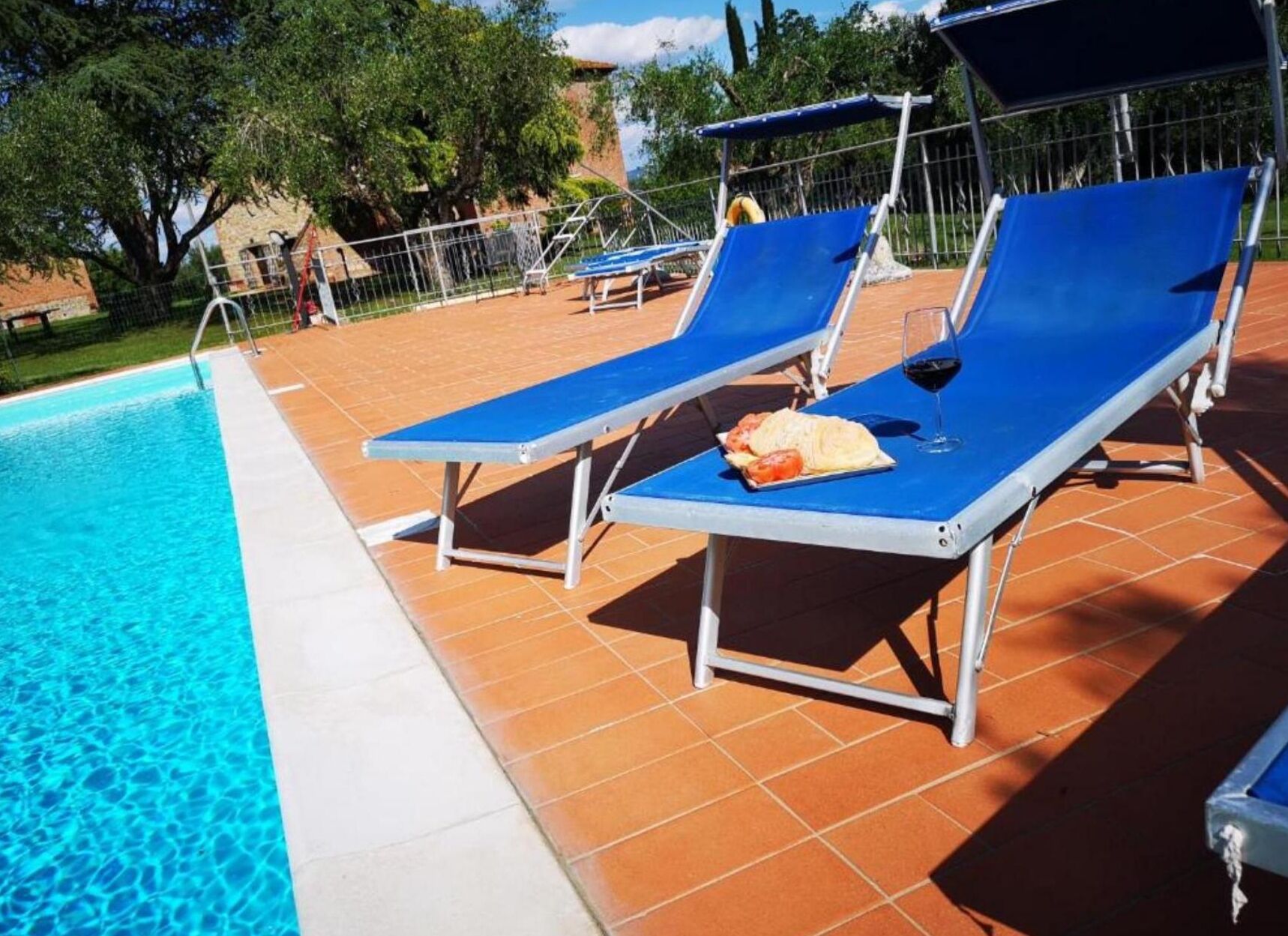 Un área junto a la piscina con tumbonas azules, un suelo de baldosas y una piscina de agua cristalina.