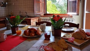A breakfast table with croissants, bread, tomatoes, and juice in a kitchen with tiled walls and a window view. - Sunflower apt With Shared Pool Family fun (Castiglione del Lago)