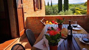 A table set outdoors with a bottle of wine, glasses, bread, and a basket of fruit. - Sunflower apt With Shared Pool Family fun (Castiglione del Lago)