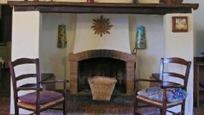A rustic fireplace with a wooden mantel, two chairs, and a woven basket. - Sunflower apt With Shared Pool Family fun (Castiglione del Lago)