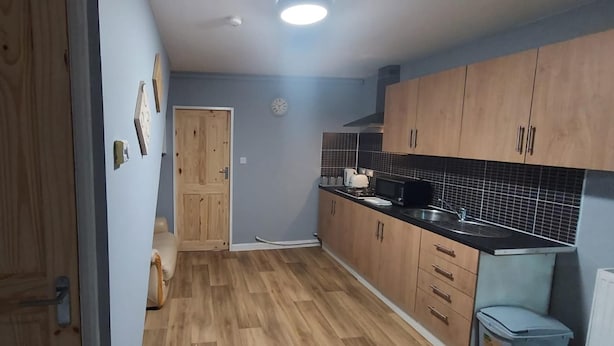 A compact kitchen with wooden cabinets, a black countertop, and a tiled backsplash. - 2 Bedrooms Apartment in Main Street Mexborough (Mexborough)