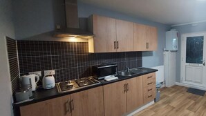 A compact kitchen with wooden cabinets, a black tiled backsplash, a microwave, and a gas stove. - 2 Bedrooms Apartment in Main Street Mexborough (Mexborough)