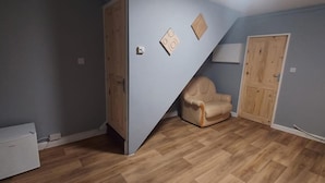A room with a wooden floor, a beige armchair, a white cabinet, and a wooden door. - 2 Bedrooms Apartment in Main Street Mexborough (Mexborough)