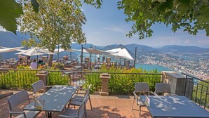 Terraza al aire libre con mesas y sillas, con vistas a una ciudad y montañas.