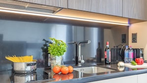 A modern kitchen with stainless steel appliances, a black countertop, and a variety of fresh produce and bottles. - Icon H 405 Suite Business (Lugano)