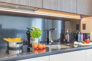A modern kitchen with stainless steel appliances, a black countertop, and a variety of fresh produce and bottles. - Icon H 405 Suite Business (Lugano)