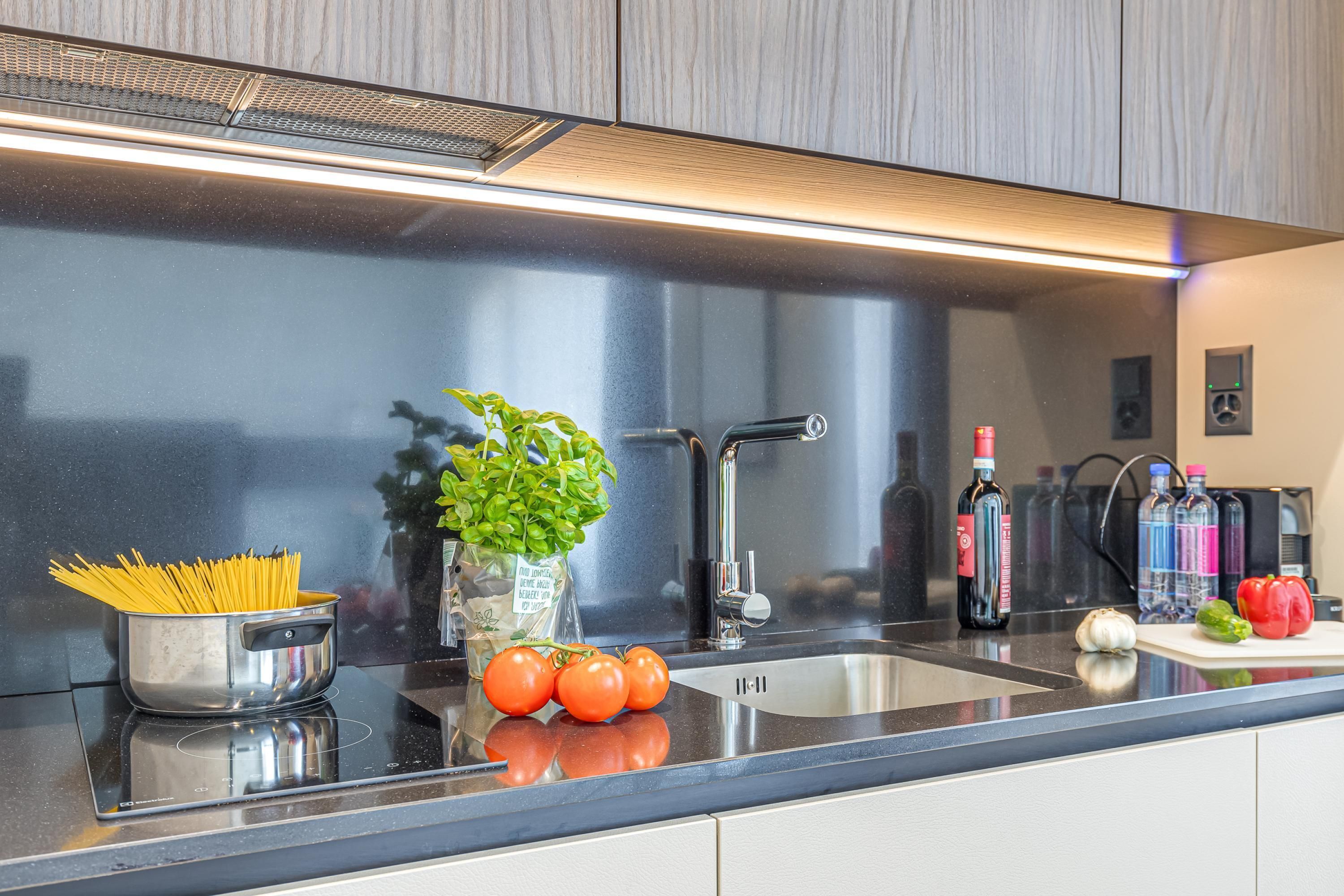 A modern kitchen with stainless steel appliances, a black countertop, and a variety of fresh produce and bottles.