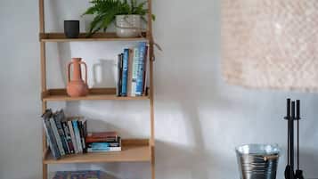 Uma estante com livros, um vaso de planta, um vaso e um balde de metal sobre uma mesa.