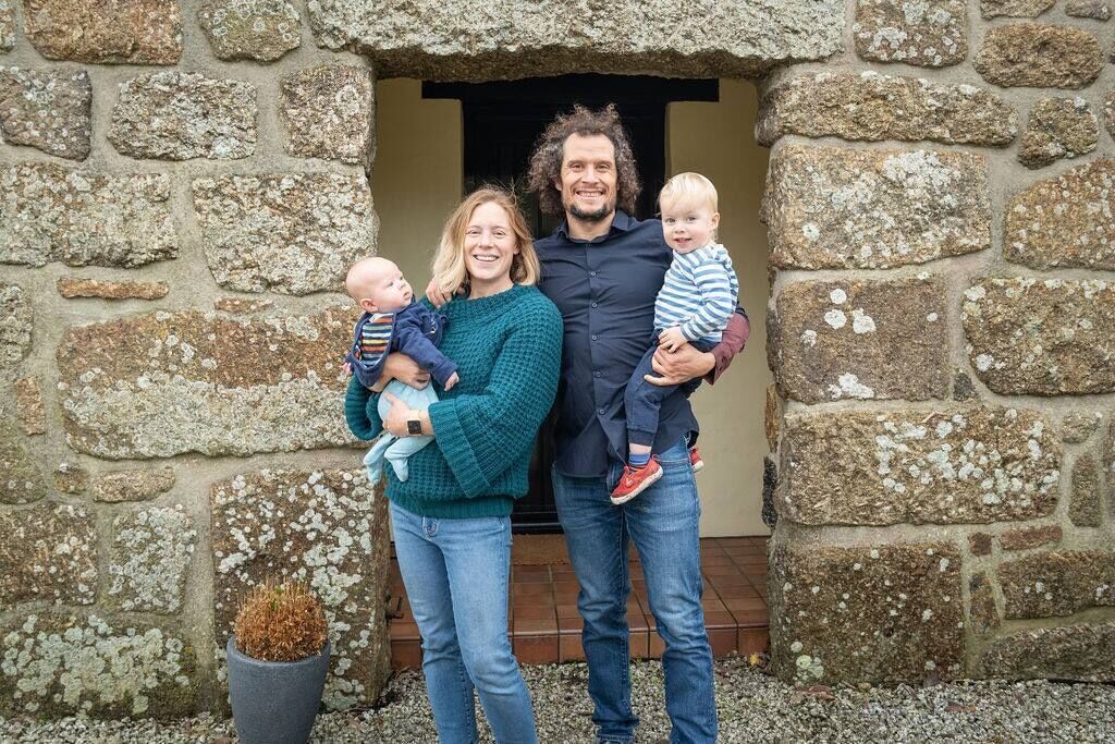 Une famille se tient devant un bâtiment en pierre, près d’une porte d’entrée.