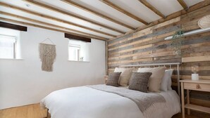 Un dormitorio con pared de listones de madera, cama con ropa de cama blanca y un tapiz de macramé.