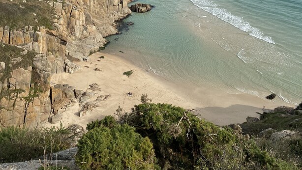 Un paisaje costero con acantilados rocosos, una playa de arena y mar tranquilo.